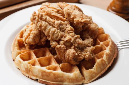 A plate featuring a golden waffle topped with crispy fried chicken pieces.