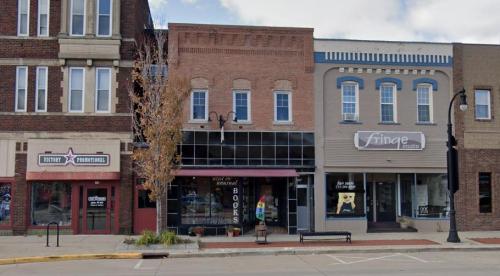 A street view of a small town with shops, including a bookstore and a studio, featuring brick and modern facades.