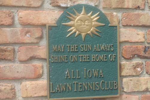 A green plaque with a sun design, reading "May the sun always shine on the home of All Iowa Lawn Tennis Club."