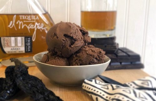 A bowl of rich chocolate ice cream with a bottle of tequila and chocolate pieces in the background.