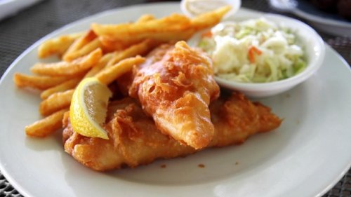 A plate of crispy fried fish fillets with lemon, served alongside fries and a side of coleslaw.