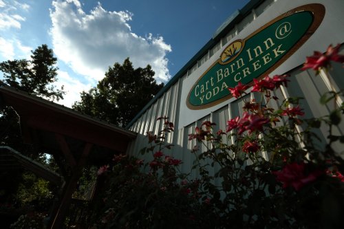 Sign for "Cart Barn Inn @ Yoda Creek" with flowers in the foreground and a blue sky with clouds in the background.
