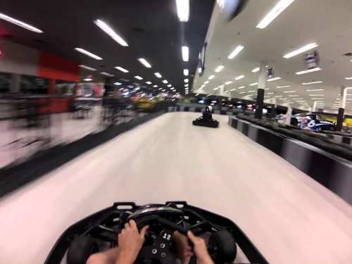 A first-person view of a go-kart racing on a track, with blurred lights and another kart in the background.