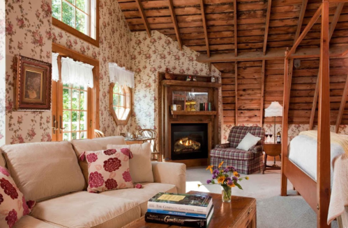 Cozy cabin interior with floral wallpaper, a fireplace, a sofa, and a plaid chair, creating a warm, inviting atmosphere.