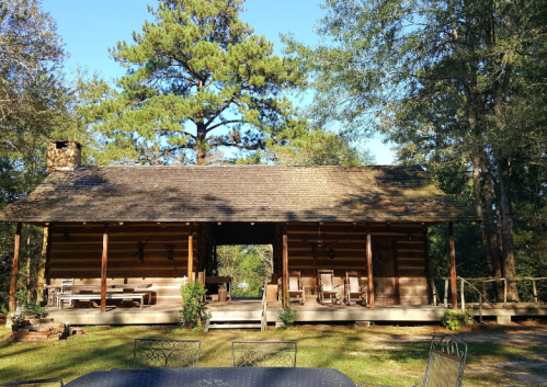 A rustic log cabin surrounded by trees, featuring a porch and rocking chairs, set in a serene outdoor environment.