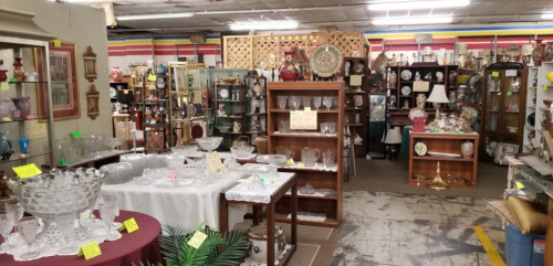 A spacious antique shop filled with glassware, furniture, and decorative items, showcasing various collectibles.