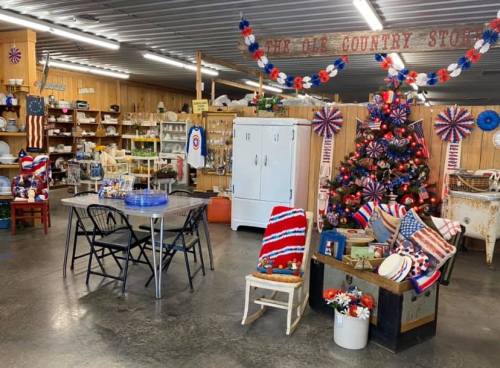 A cozy country store display with patriotic decor, a Christmas tree, and a seating area featuring red, white, and blue accents.