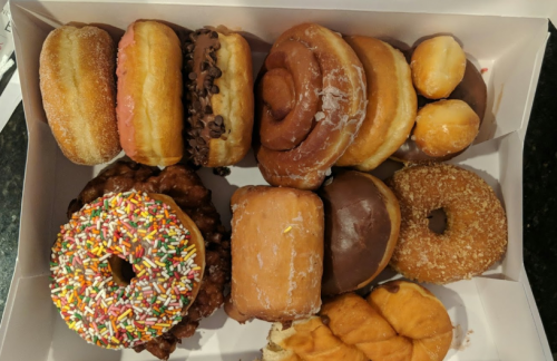 A box of assorted donuts, including glazed, chocolate, and a colorful sprinkle donut.