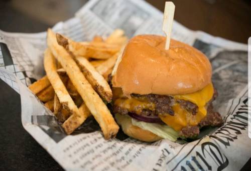 A juicy cheeseburger with lettuce and onion, served with crispy French fries in a paper-lined basket.