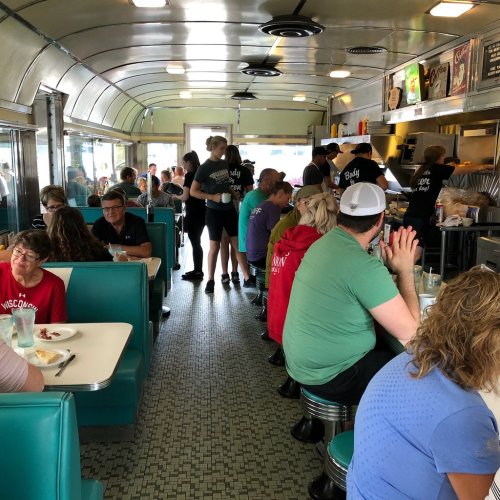 A busy diner interior with patrons at booths and a counter, servers taking orders, and a retro atmosphere.