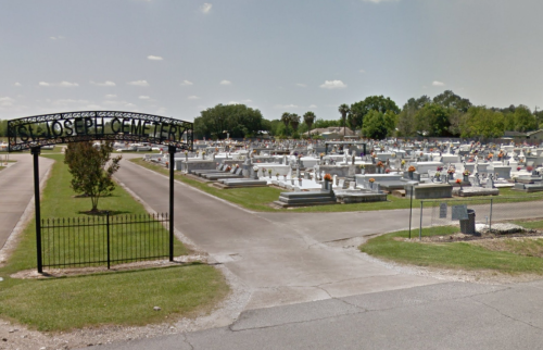 Entrance to St. Joseph Cemetery, featuring rows of gravestones and a clear blue sky.