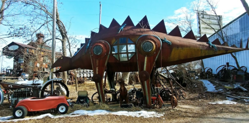 A whimsical, large metal sculpture resembling a creature, surrounded by vintage machinery and a red toy car.