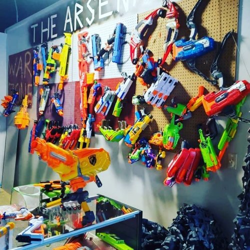 A colorful display of various toy blasters and Nerf guns arranged on a wall with a sign reading "The Arsenal."