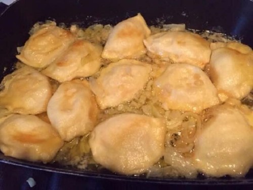 A skillet filled with golden-brown fried dumplings, sizzling in oil with some onions visible.