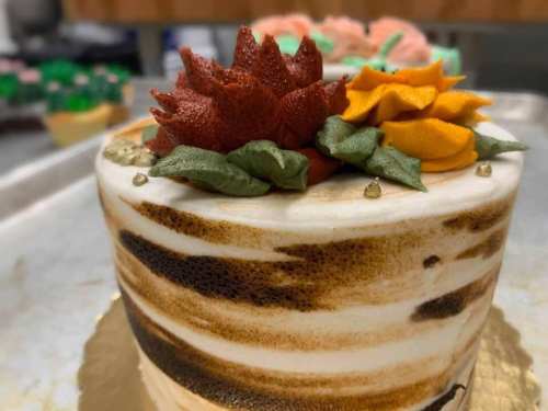 A beautifully decorated cake with intricate floral designs in red and orange, set on a gold base.