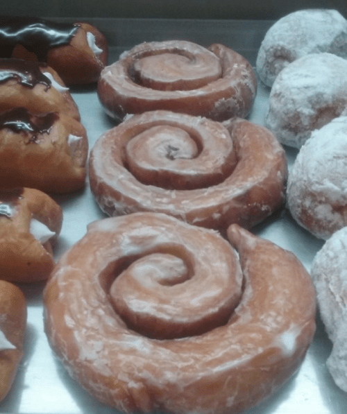 A display of various pastries, including glazed cinnamon rolls and powdered donuts, arranged on a tray.