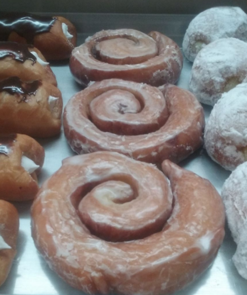 A display of various pastries, including glazed cinnamon rolls and powdered donuts, arranged on a tray.