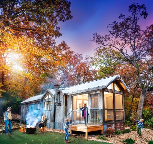 A cozy cabin surrounded by autumn trees, with a family gathered around a fire pit, enjoying the outdoors.
