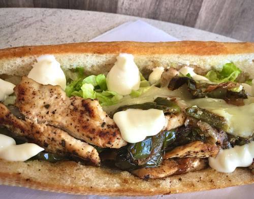 A close-up of a sandwich filled with grilled chicken, peppers, lettuce, and mayonnaise on a toasted bun.