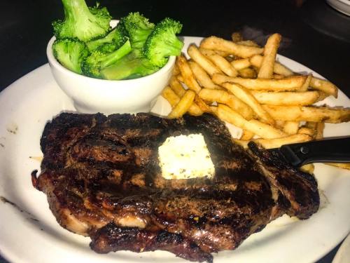 A plate featuring a grilled steak with a pat of butter, served with fries and a side of steamed broccoli.