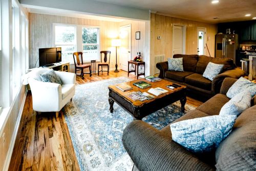Cozy living room with brown sofas, a coffee table, a TV, and large windows, featuring a light rug and wooden floors.