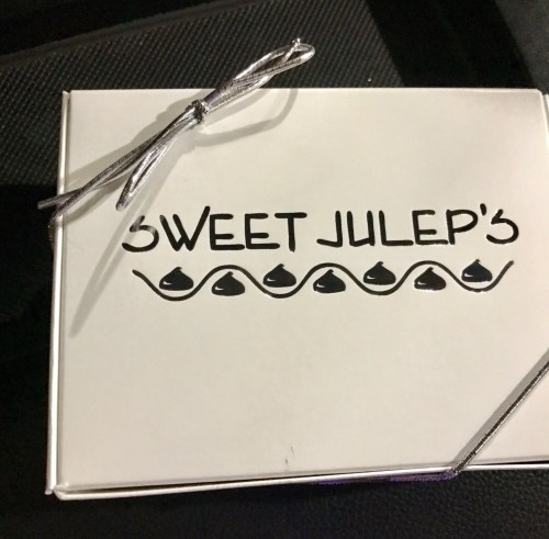 A white box tied with a silver ribbon, featuring the text "SWEET JULEP'S" and decorative designs.