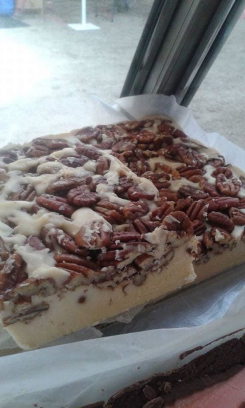 A rectangular dessert topped with pecans and a creamy frosting, displayed on a white surface near a window.