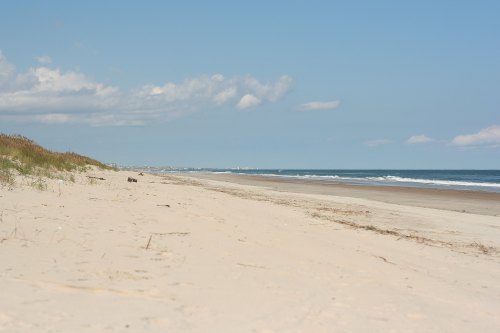 A serene beach scene with soft sand, gentle waves, and a clear blue sky dotted with clouds.