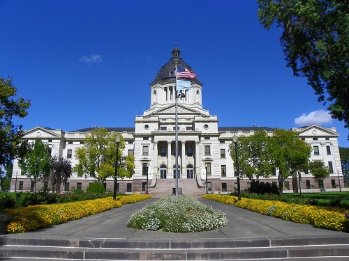 Historic building with a dome, surrounded by colorful flowers and trees, under a clear blue sky.