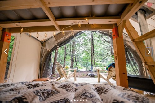 Cozy interior of a tent with a view of wooden chairs and trees outside, adorned with string lights.