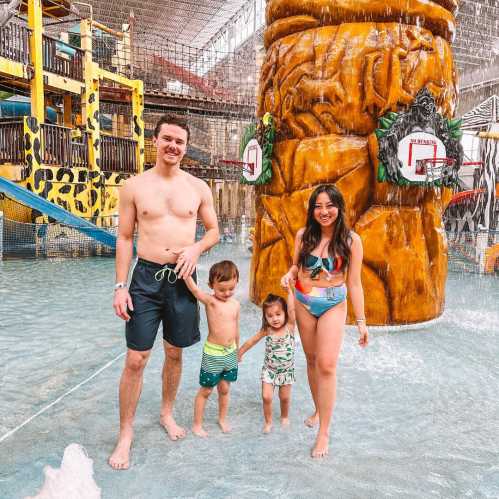 A family of four enjoys a water park, standing in shallow water near a large, colorful water feature.