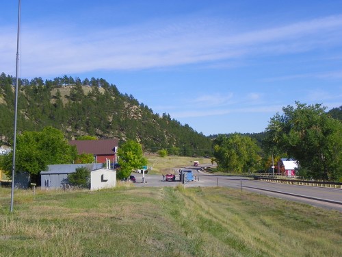 A scenic view of a highway winding through a rural area with trees and hills, featuring a few buildings nearby.