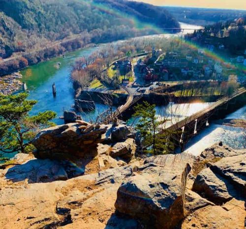 A scenic view from a rocky overlook, showcasing a river, a bridge, and a small town surrounded by lush greenery.