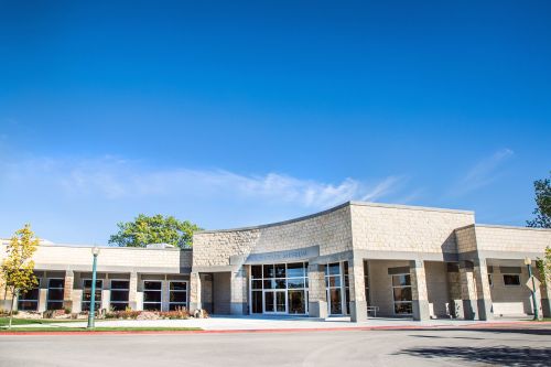 Modern museum building with stone facade, large windows, and clear blue sky. Trees and landscaped area in front.