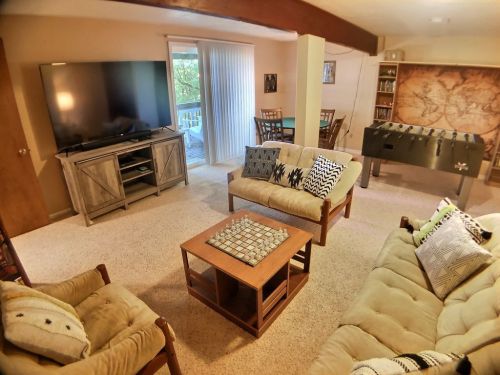 Cozy living room with a large TV, seating area, coffee table, and a foosball table in a bright, inviting space.