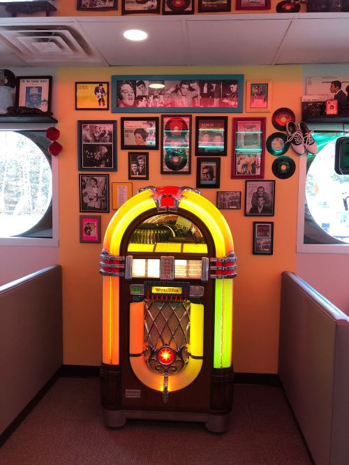 A colorful vintage jukebox stands against a wall adorned with framed photos and records in a retro diner setting.