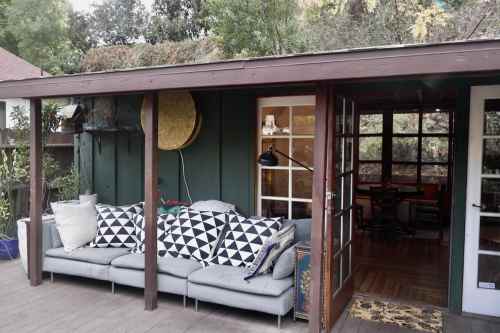 Cozy outdoor seating area with a gray sofa, patterned pillows, and a green wall, surrounded by greenery.