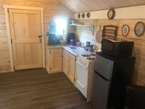 Cozy kitchen with wooden walls, featuring a stove, sink, microwave, and a water dispenser.