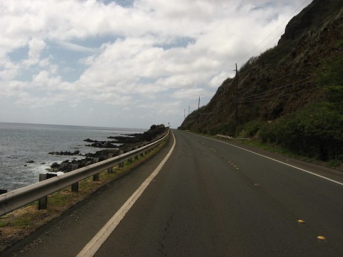 A winding coastal road alongside rocky shores and the ocean under a cloudy sky.