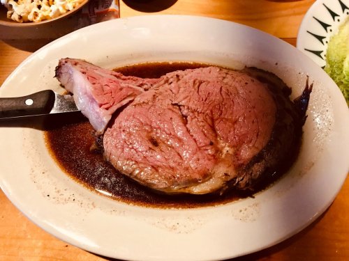 A large, juicy prime rib roast served on a platter with a knife, surrounded by a rich brown sauce.
