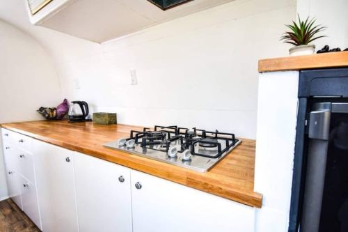 A modern kitchen with a wooden countertop, gas stove, and white cabinets, featuring a kettle and small plant.
