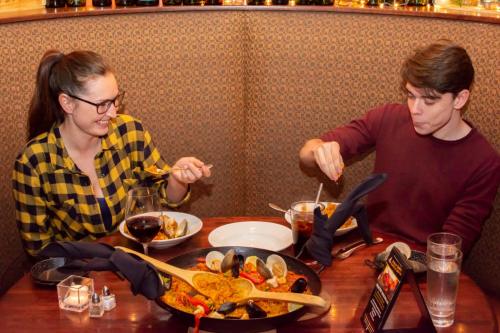 A man and woman enjoy a meal at a restaurant, sharing a large dish and drinks, smiling and engaged in conversation.
