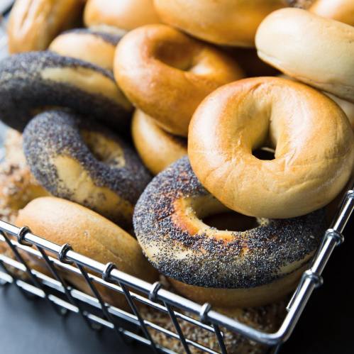 A basket filled with various bagels, including poppy seed and plain, arranged closely together.