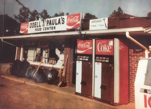 A vintage storefront of Odell & Paula's Food Center with Coca-Cola signage and vending machines outside.