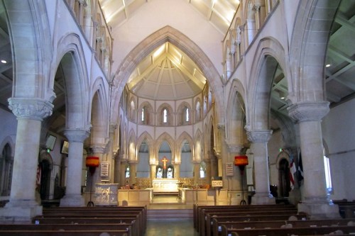 Interior of a church featuring tall arches, wooden pews, and an altar with a cross, illuminated by soft lighting.