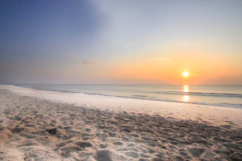 A serene beach at sunset, with gentle waves lapping at the shore and a warm glow in the sky.