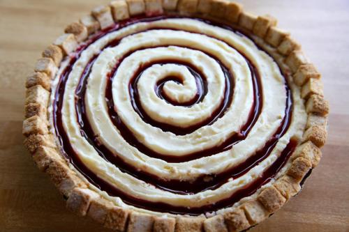 A pie with a spiral design of cream and fruit filling in a golden crust, placed on a wooden surface.