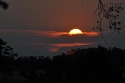 A sunset peeks through clouds, casting a warm glow over a silhouette of trees against a darkening sky.
