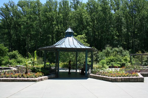 A gazebo surrounded by vibrant gardens and lush greenery on a sunny day.