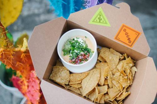 A takeout box filled with tortilla chips and a small cup of salsa topped with chopped onions and cilantro.